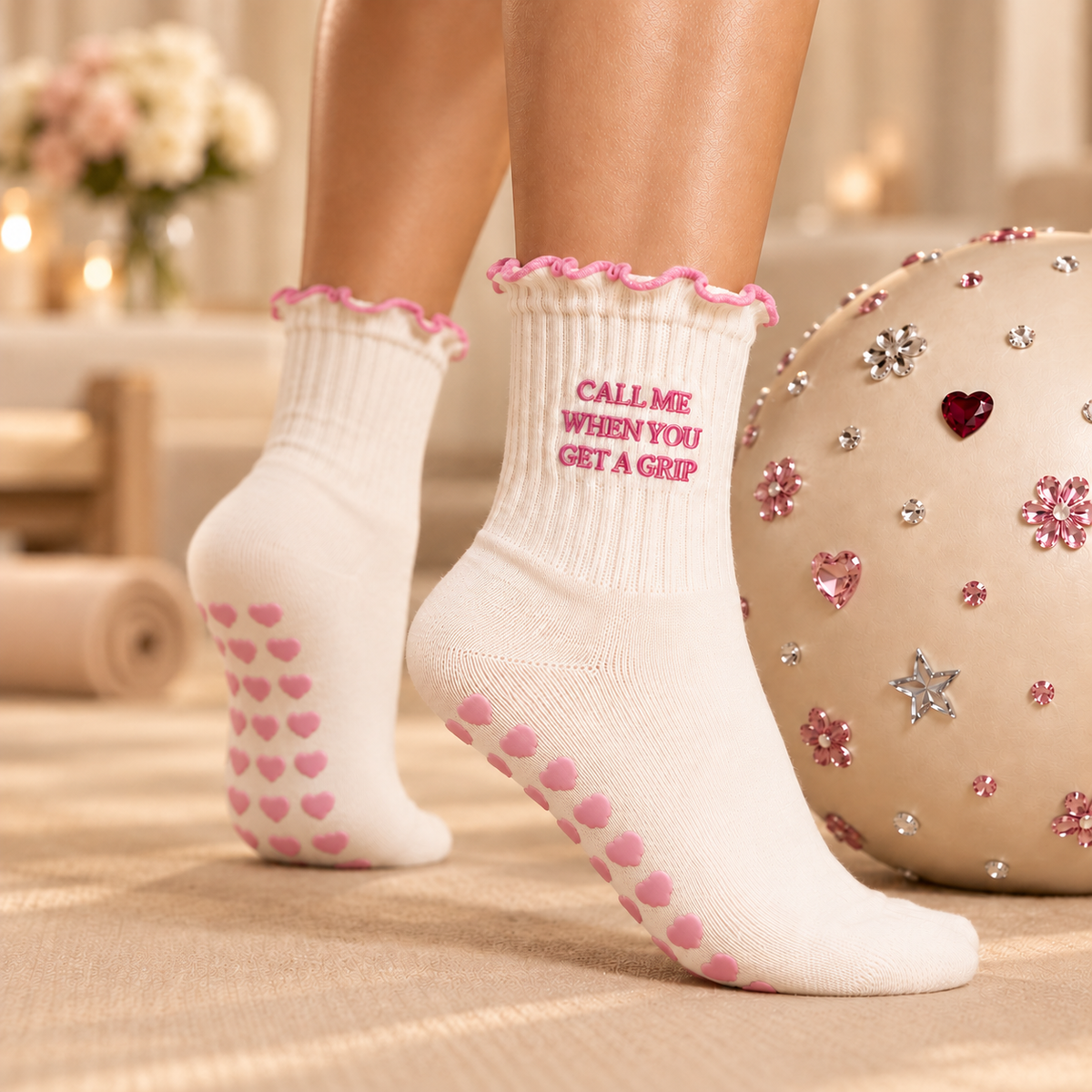 Two cream Pilates socks with pink cloud grips beside jeweled Pilates ball